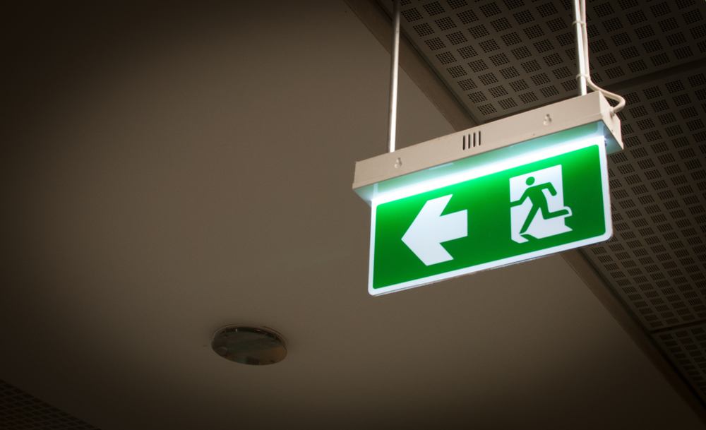 Green,Fire,Escape,Sign,Hanging,From,Ceiling,With,Arrow,Direction.